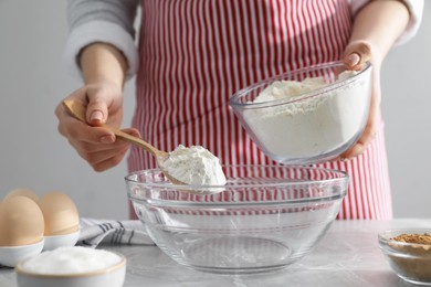 Photo of Making cinnamon rolls. Woman adding flour into bowl at gray marble table, closeup