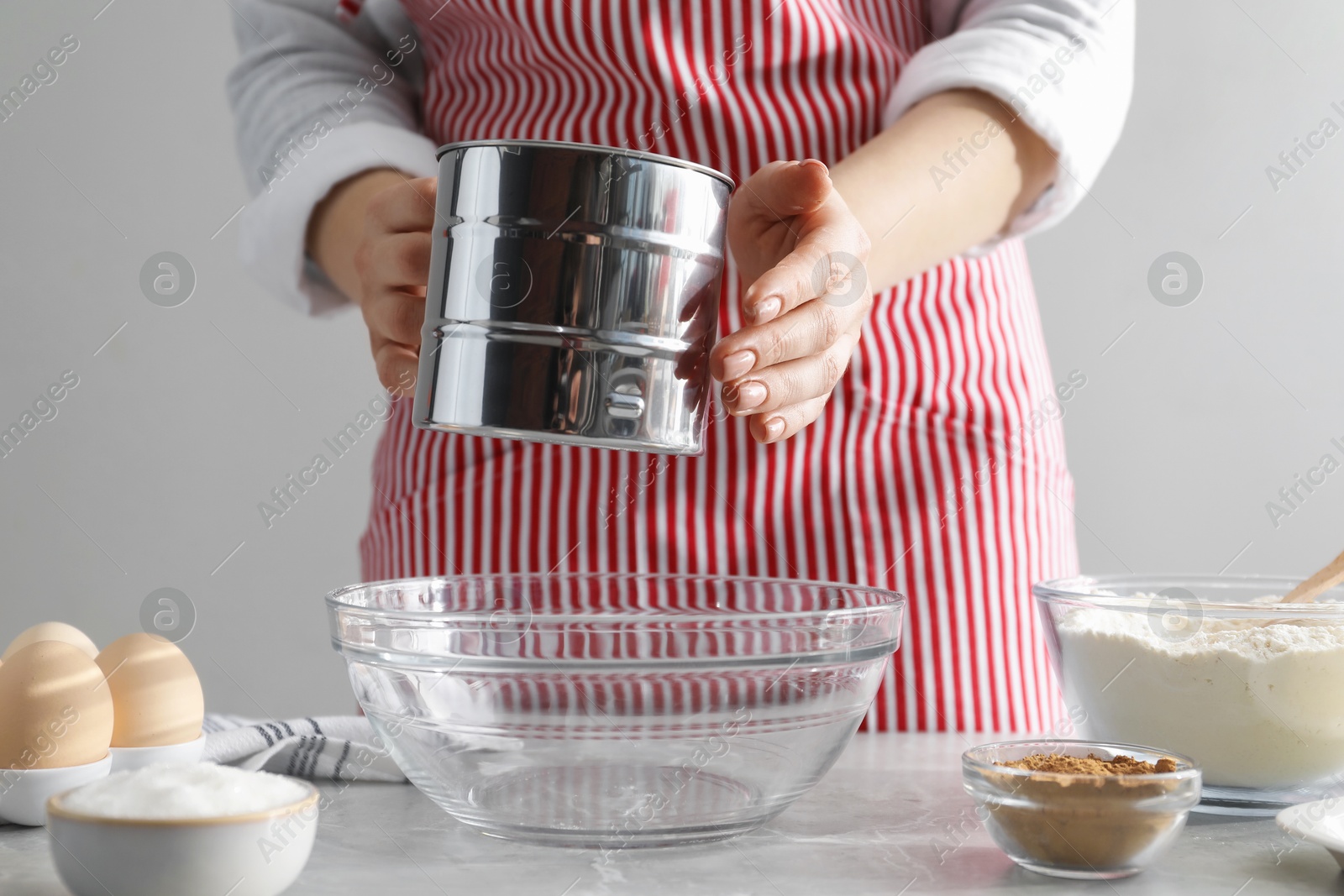 Photo of Making cinnamon rolls. Woman sieving flour at gray marble table, closeup