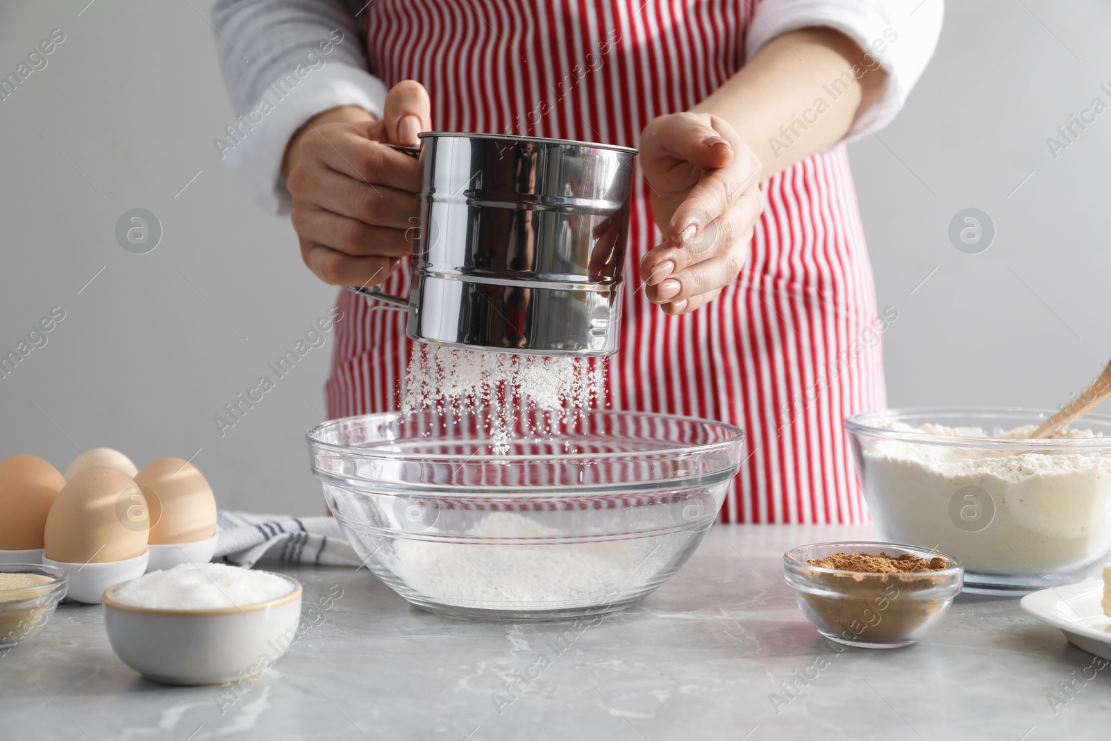 Photo of Making cinnamon rolls. Woman sieving flour at gray marble table, closeup