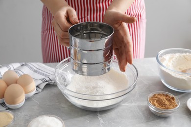 Photo of Making cinnamon rolls. Woman sieving flour at gray marble table, closeup