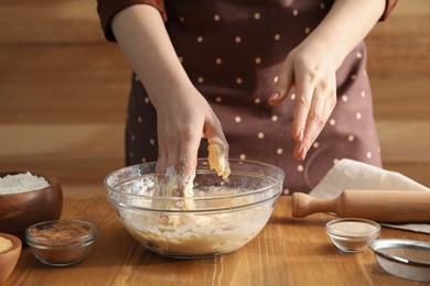 Photo of Woman kneading dough for cinnamon rolls at wooden table, closeup