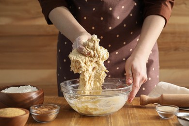 Photo of Woman kneading dough for cinnamon rolls at wooden table, closeup