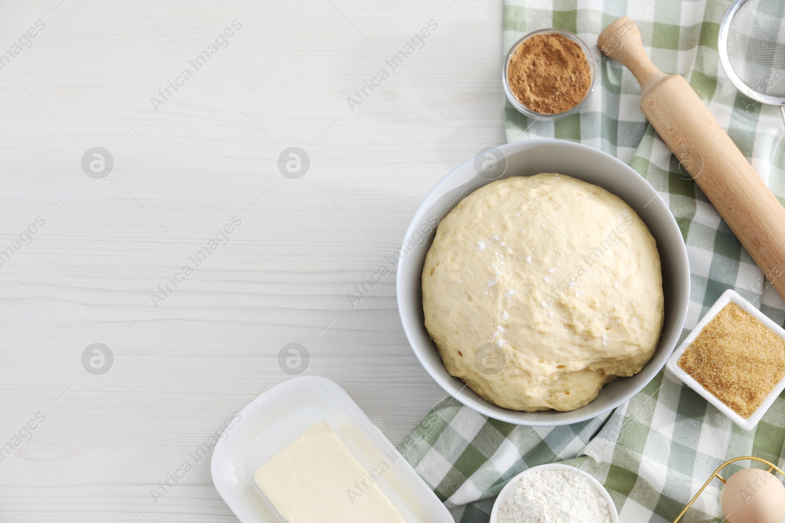 Photo of Making cinnamon rolls. Fresh dough in bowl, ingredients and rolling pin on light wooden table, flat lay. Space for text