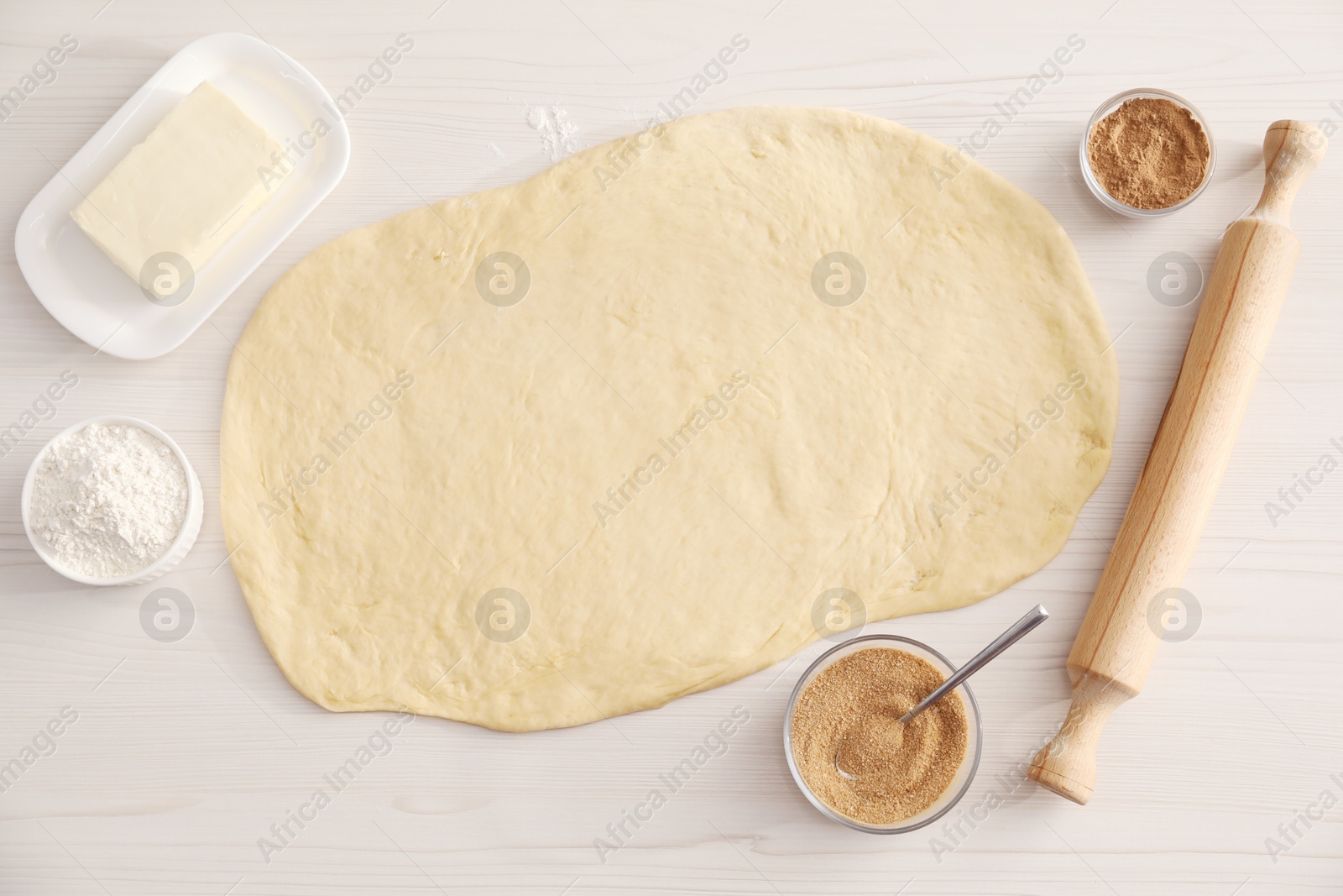 Photo of Making cinnamon rolls. Dough, other ingredients and rolling pin on white wooden table, flat lay