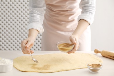 Photo of Making cinnamon rolls. Woman adding spice with sugar into dough at white wooden table, closeup