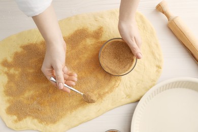 Photo of Making cinnamon rolls. Woman adding spice, with sugar into dough at white wooden table, top view