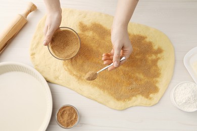 Photo of Making cinnamon rolls. Woman adding spice, with sugar into dough at white wooden table, top view