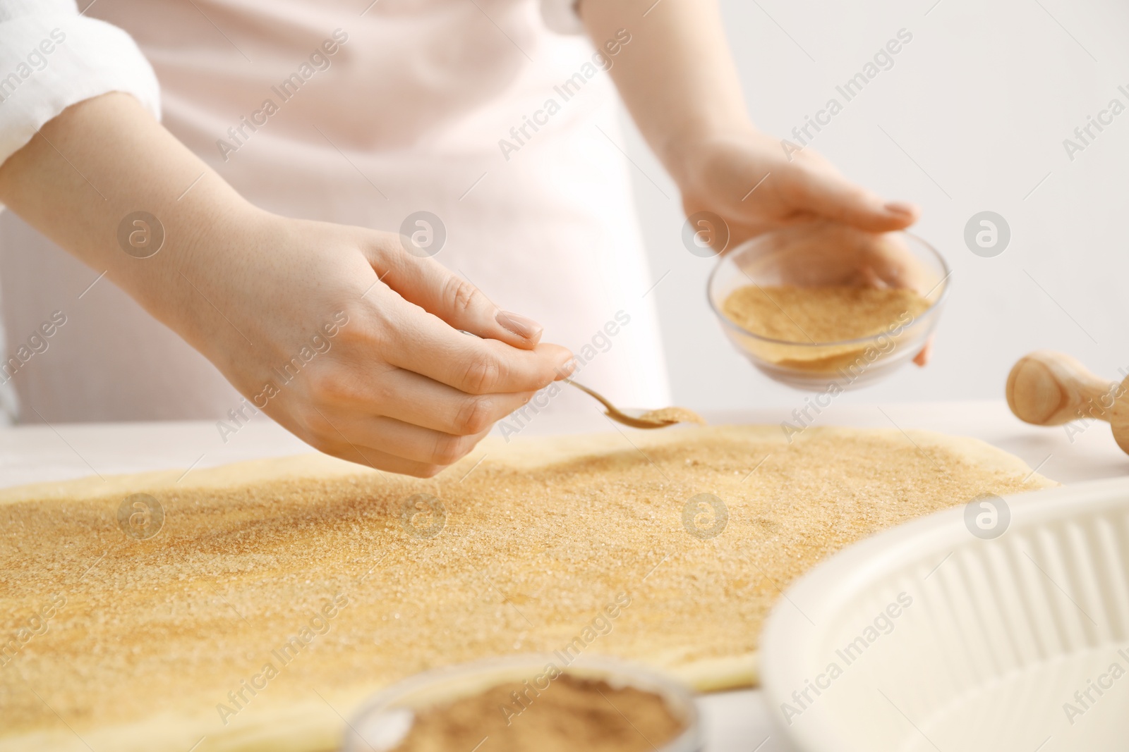 Photo of Making cinnamon rolls. Woman adding spice with sugar into dough at table, closeup