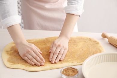 Photo of Making cinnamon rolls. Woman with dough at white wooden table, closeup