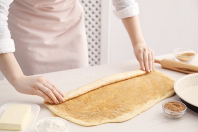 Photo of Making cinnamon rolls. Woman shaping dough at white wooden table, closeup