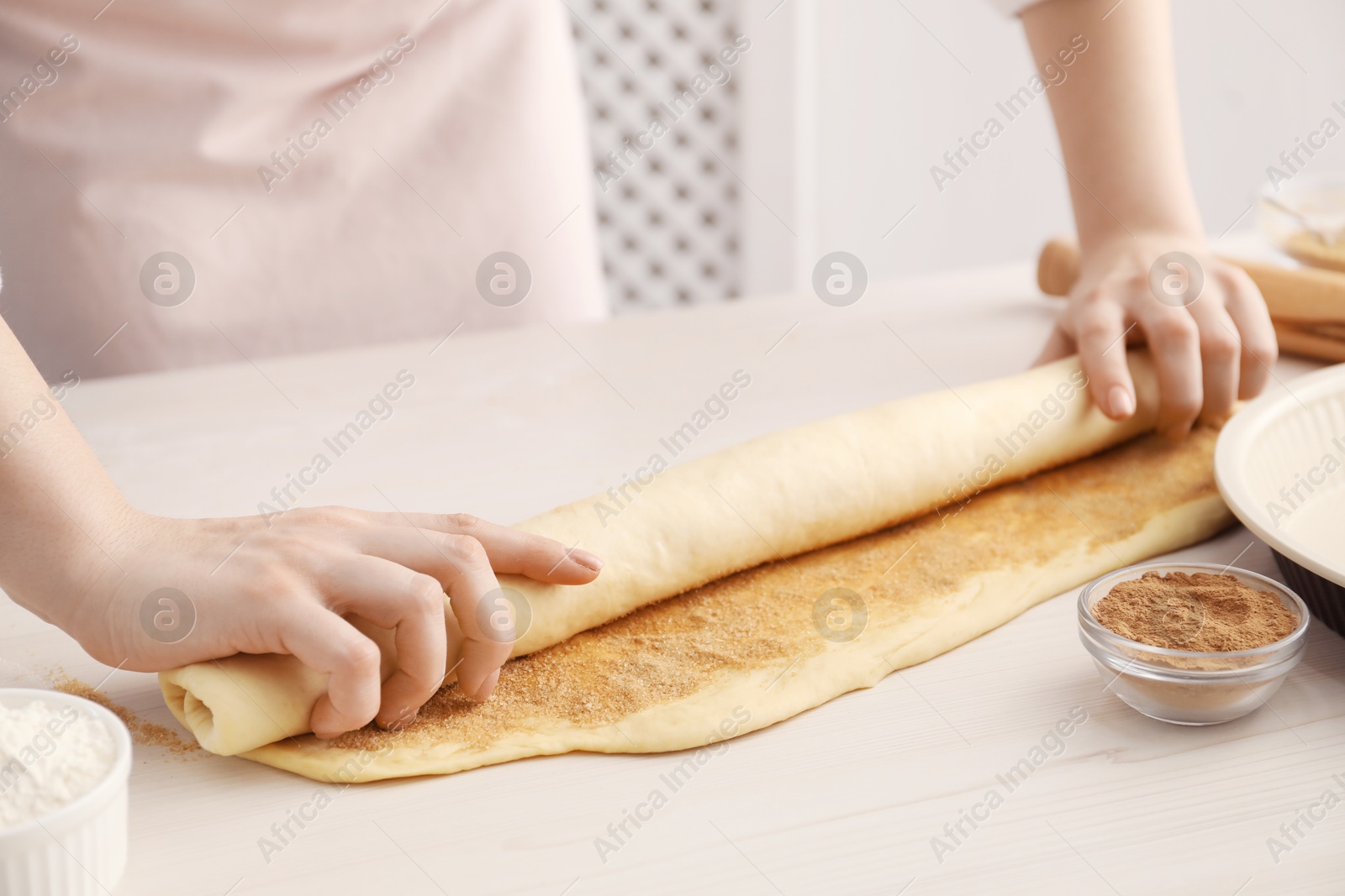 Photo of Making cinnamon rolls. Woman shaping dough at white wooden table, closeup