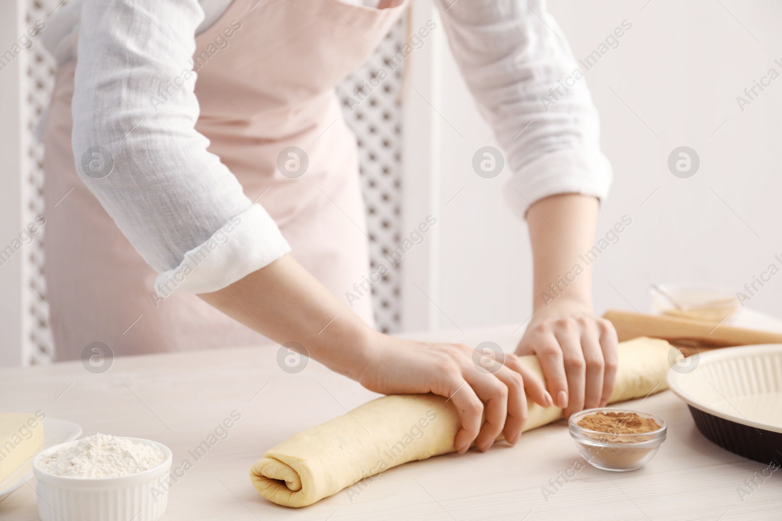 Photo of Making cinnamon rolls. Woman shaping dough at white wooden table, closeup