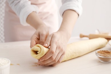 Photo of Making cinnamon rolls. Woman shaping dough at white wooden table, closeup