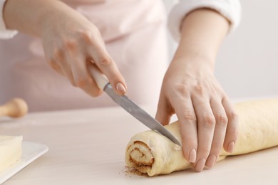 Photo of Making cinnamon rolls. Woman cutting dough at white wooden table, closeup