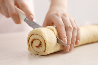 Photo of Making cinnamon rolls. Woman cutting dough at white wooden table, closeup