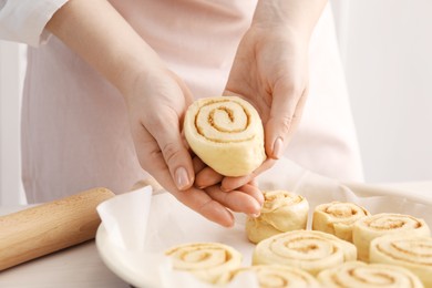 Photo of Woman putting cinnamon roll into baking dish at table, closeup