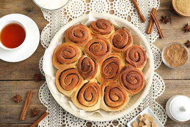 Photo of Freshly baked cinnamon rolls, tea and spices on wooden table, flat lay