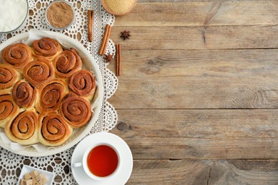 Photo of Freshly baked cinnamon rolls, tea and spices on wooden table, flat lay. Space for text