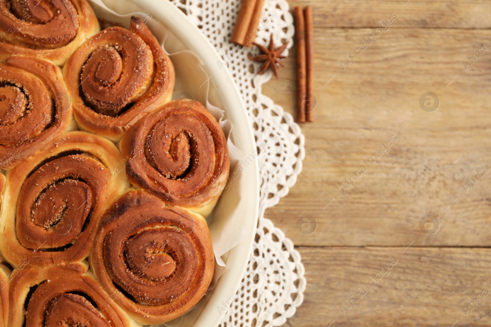 Photo of Freshly baked cinnamon rolls and spices on wooden table, flat lay. Space for text