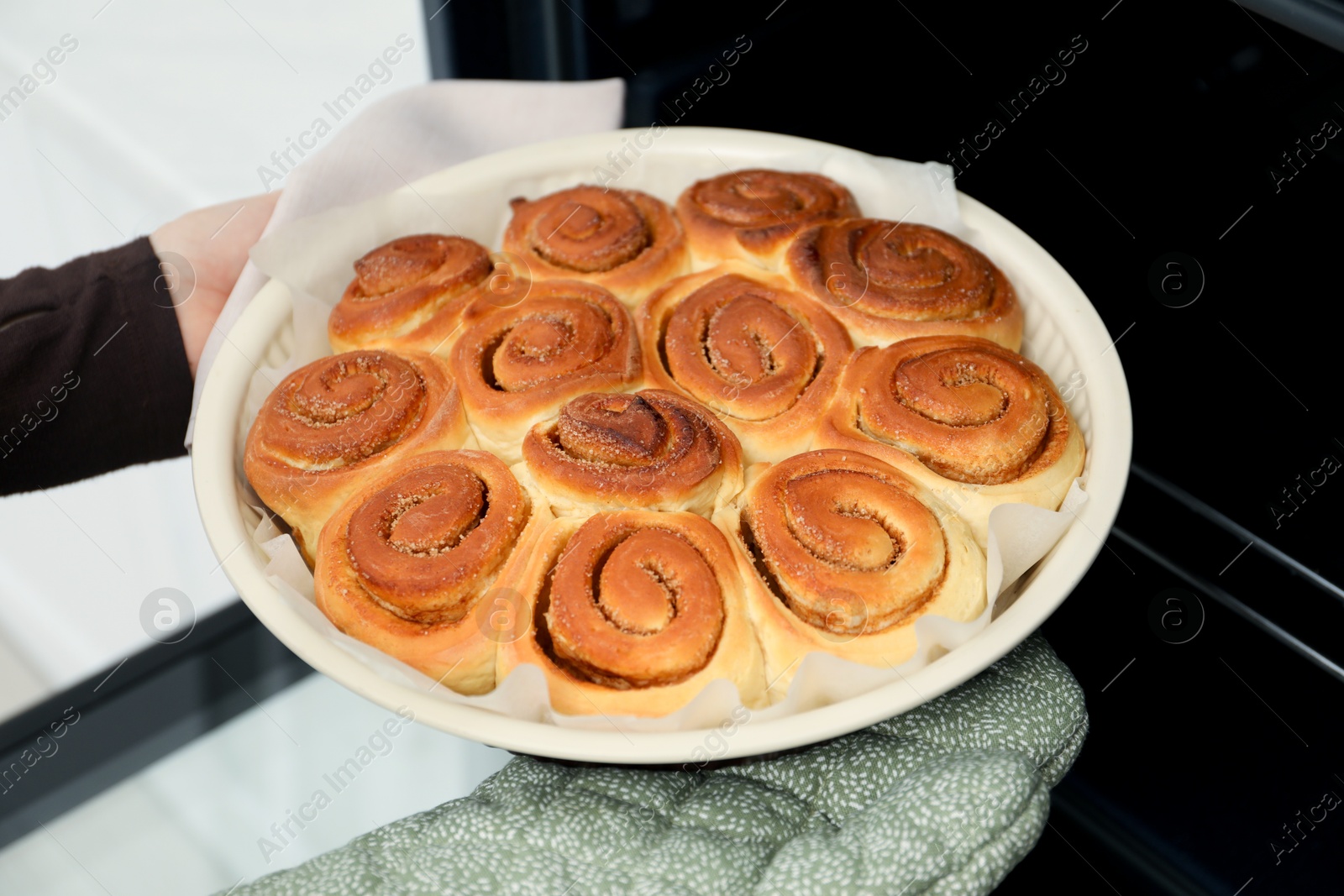 Photo of Woman taking delicious cinnamon rolls out of oven, closeup