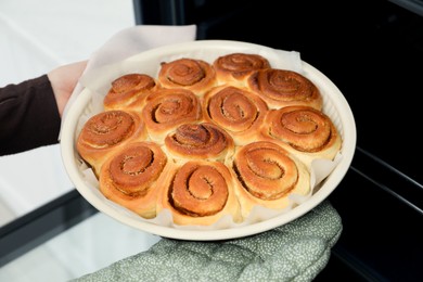 Photo of Woman taking delicious cinnamon rolls out of oven, closeup