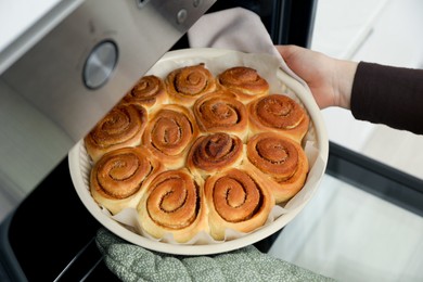 Photo of Woman taking delicious cinnamon rolls out of oven, closeup