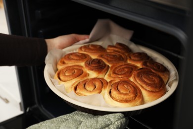 Photo of Woman taking delicious cinnamon rolls out of oven, closeup