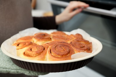 Photo of Woman with delicious cinnamon rolls near oven indoors, closeup