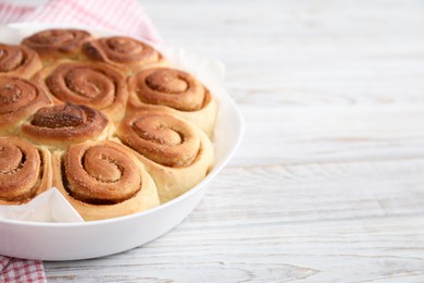 Photo of Freshly baked cinnamon rolls on light wooden table, closeup. Space for text