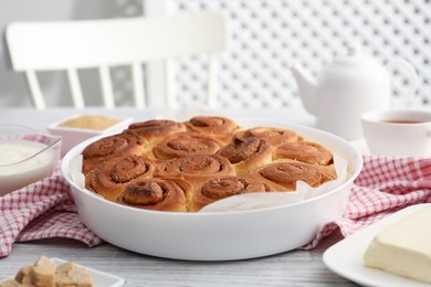 Photo of Freshly baked cinnamon rolls and ingredients on light wooden table indoors, closeup