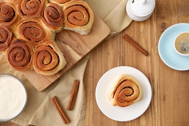 Photo of Freshly baked cinnamon rolls, spices and coffee on wooden table, flat lay