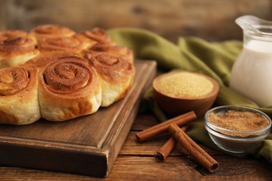 Photo of Freshly baked cinnamon rolls and spices on wooden table, closeup