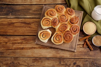 Photo of Freshly baked cinnamon rolls, milk and spices on wooden table, flat lay. Space for text