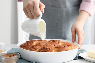 Photo of Woman with freshly baked cinnamon rolls and pitcher at white table indoors, closeup