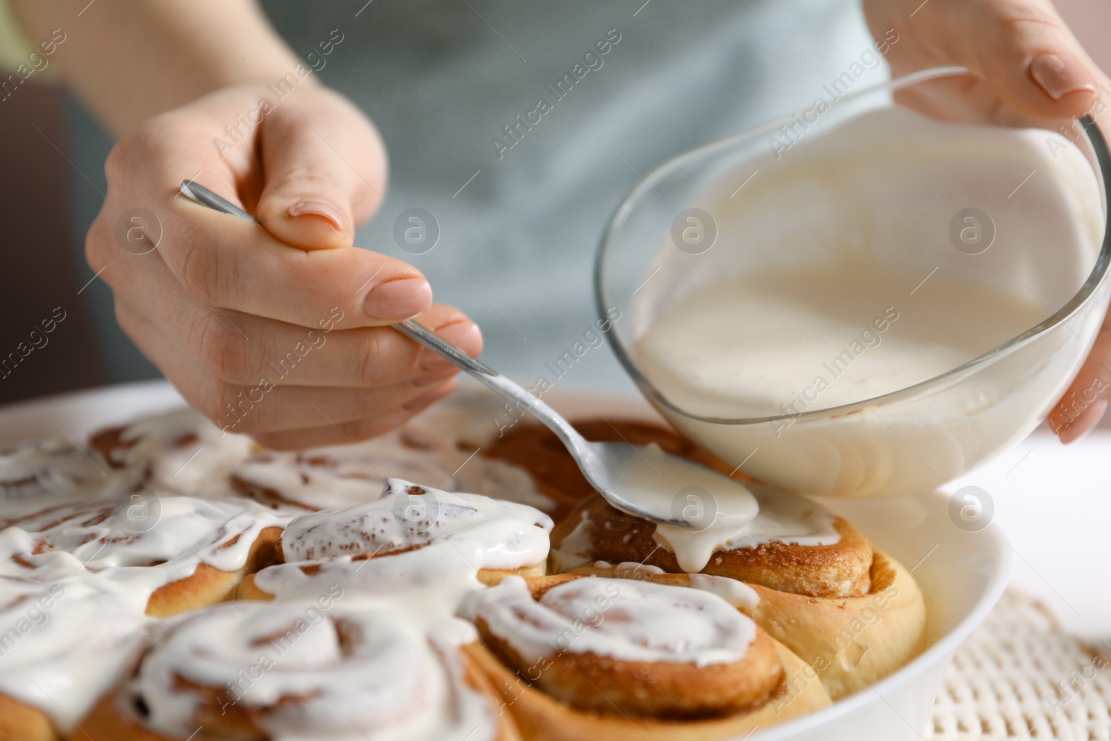 Photo of Woman spreading frosting onto freshly baked cinnamon rolls at white table, closeup