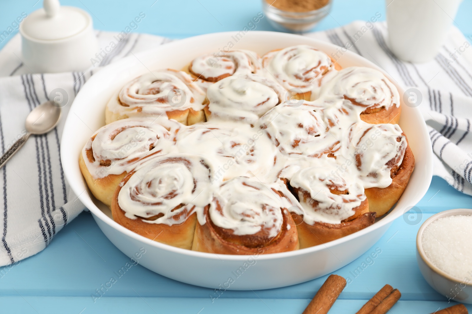 Photo of Delicious frosted cinnamon rolls in baking dish on light blue wooden table, closeup