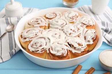 Photo of Delicious frosted cinnamon rolls in baking dish on light blue wooden table, closeup