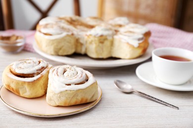 Photo of Delicious frosted cinnamon rolls on light wooden table, closeup