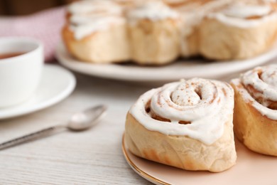 Photo of Delicious frosted cinnamon rolls on light wooden table, closeup