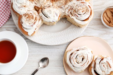 Photo of Delicious frosted cinnamon rolls and tea on light wooden table, flat lay