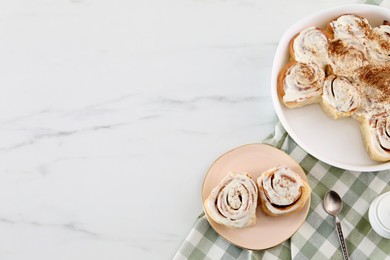 Photo of Delicious frosted cinnamon rolls on white marble table, top view. Space for text