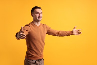 Photo of Cheerful man welcoming guests on orange background