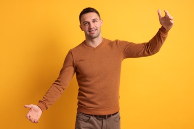 Photo of Cheerful man welcoming guests on orange background