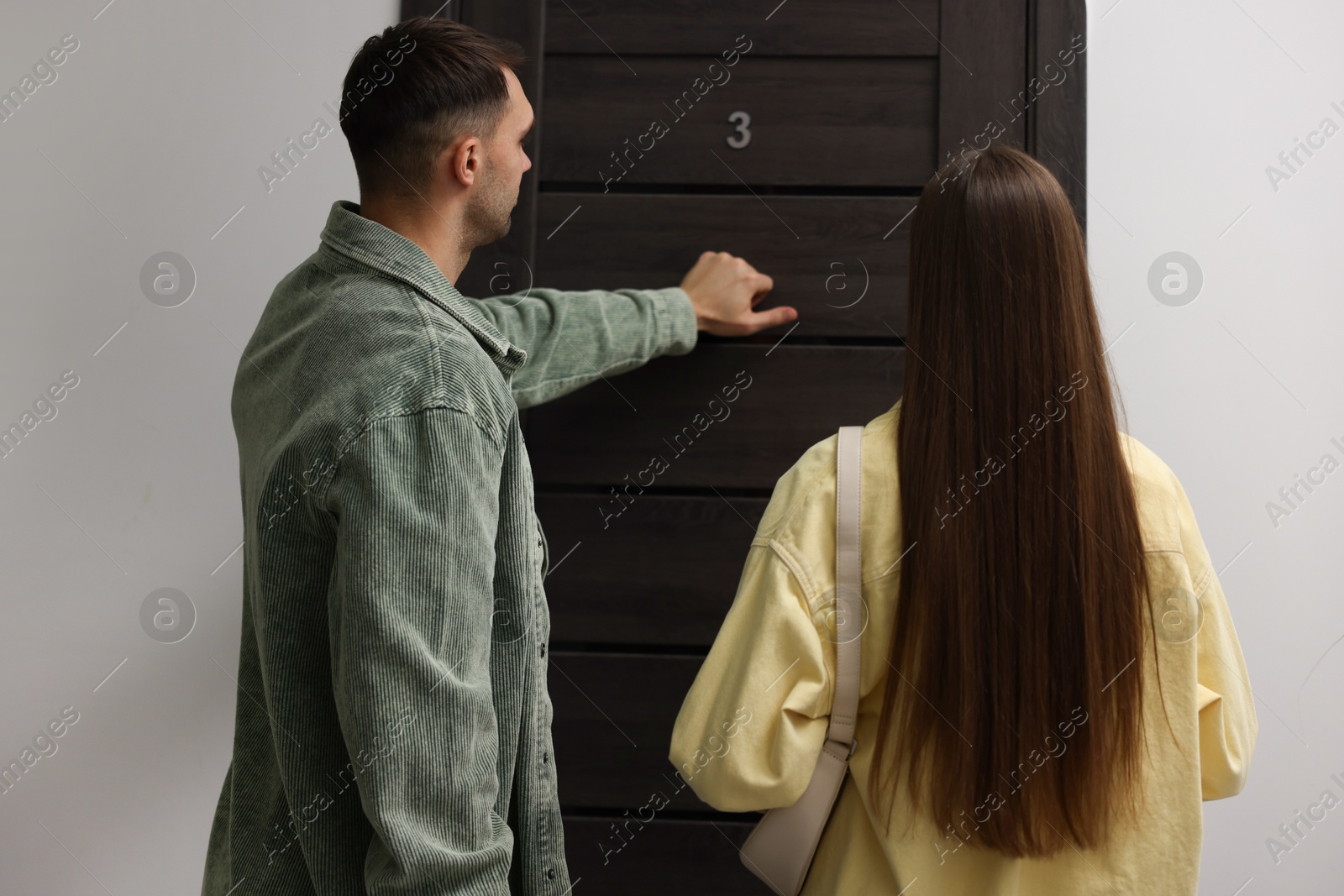 Photo of Couple knocking on door of their neighbors apartment, back view