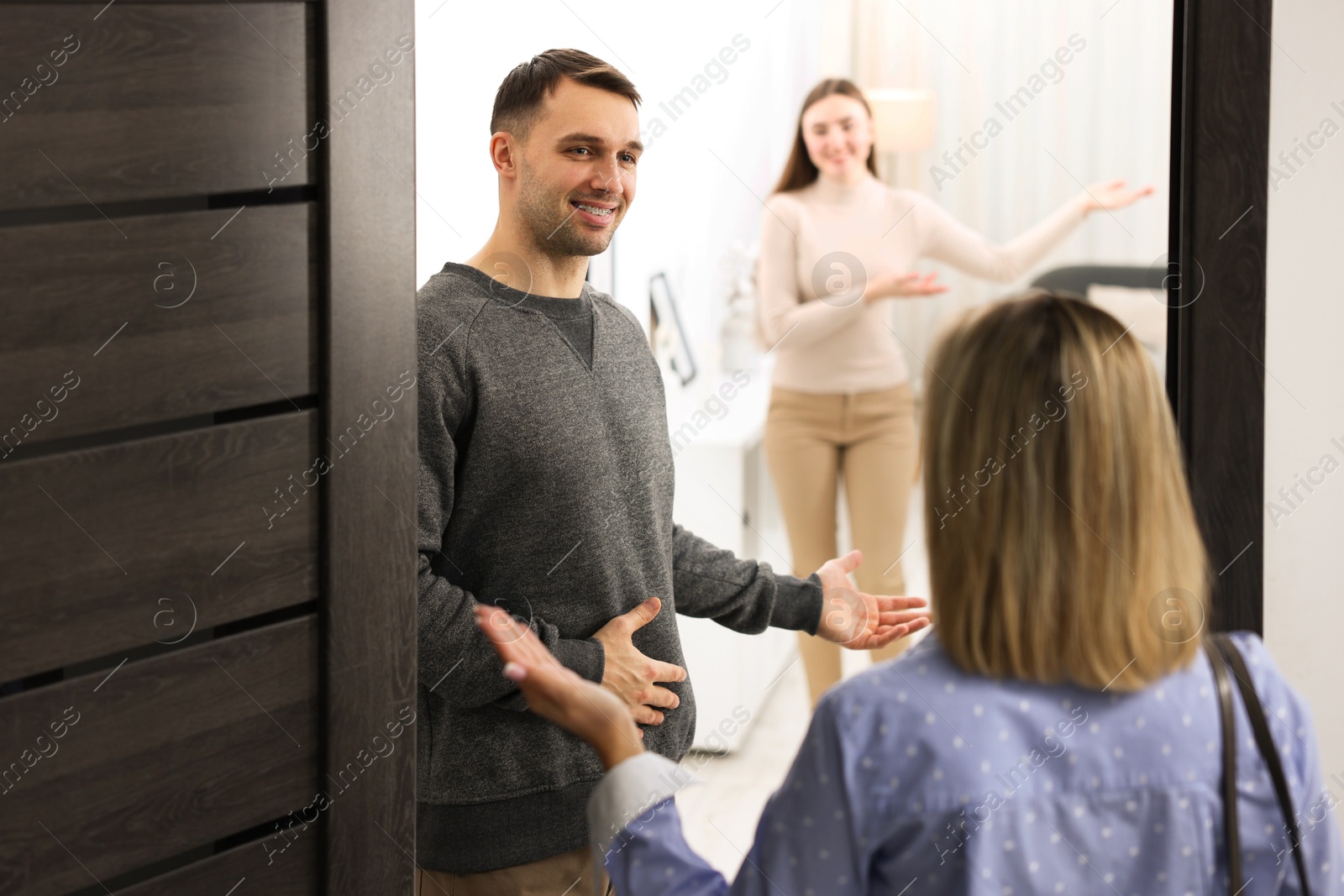 Photo of Lovely couple welcoming friend to their apartment, selective focus