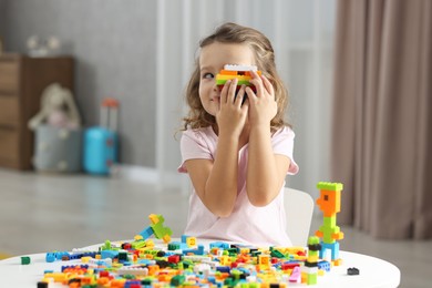 Photo of Cute girl playing with building blocks at white table indoors