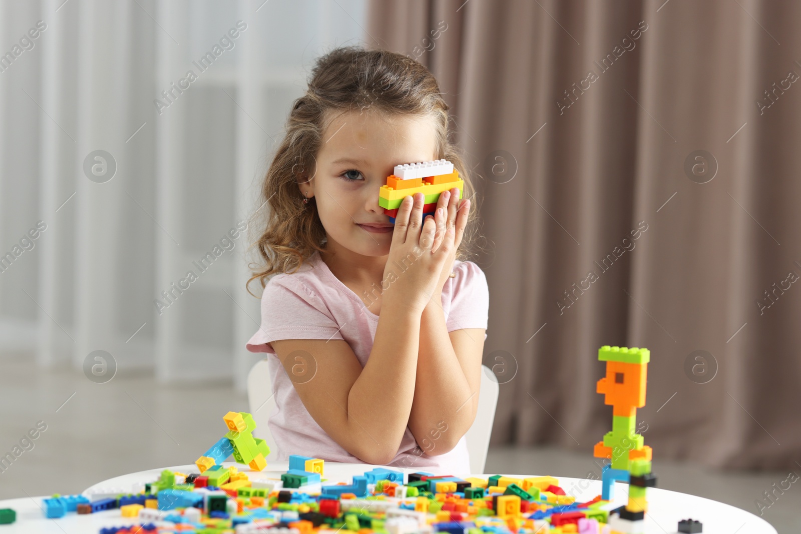 Photo of Cute girl playing with building blocks at white table indoors