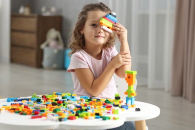 Photo of Cute girl playing with building blocks at white table indoors