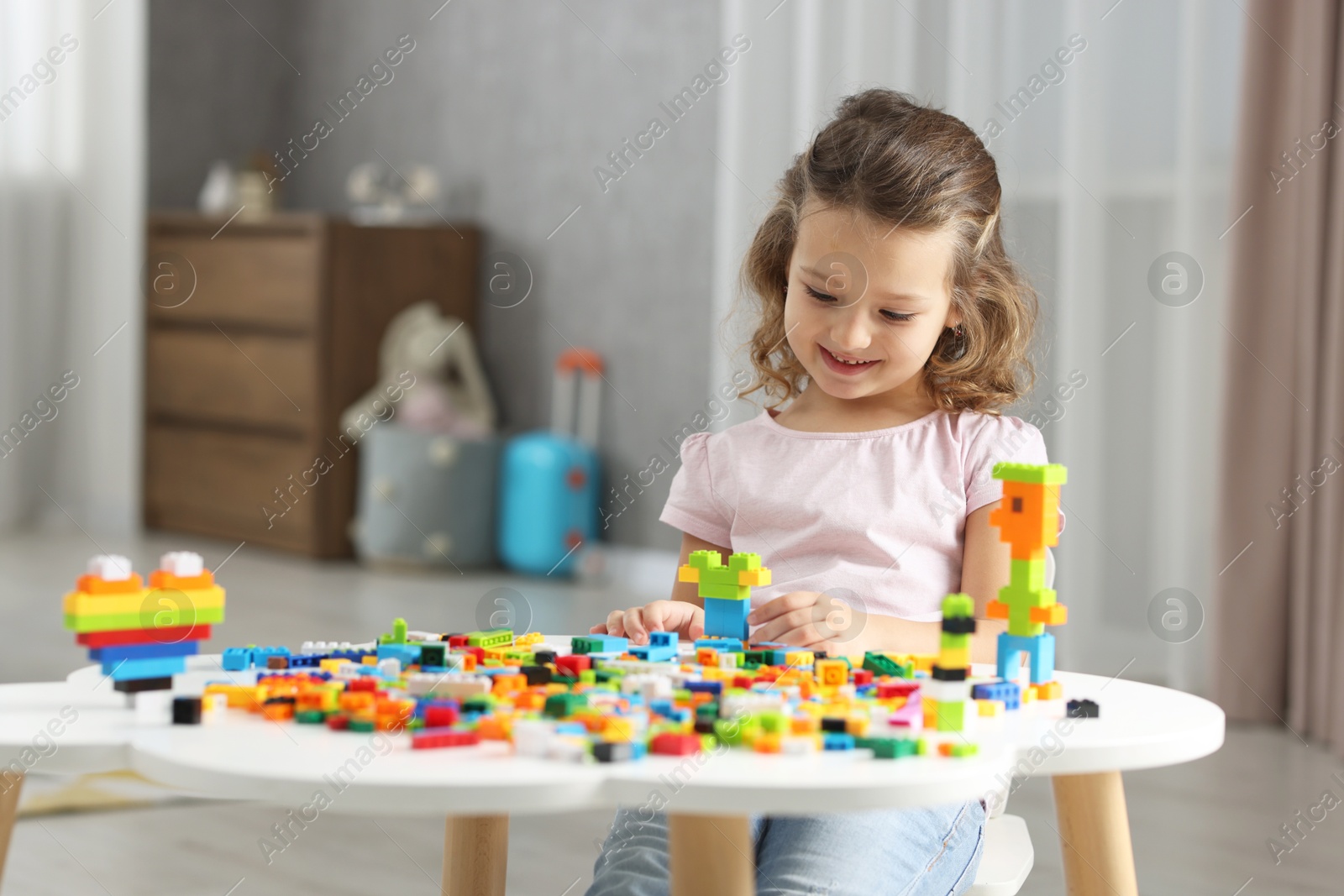 Photo of Cute girl playing with building blocks at white table indoors