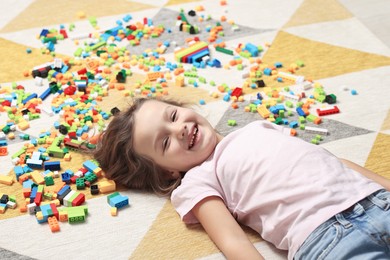 Photo of Cute girl lying near building blocks on carpet at home